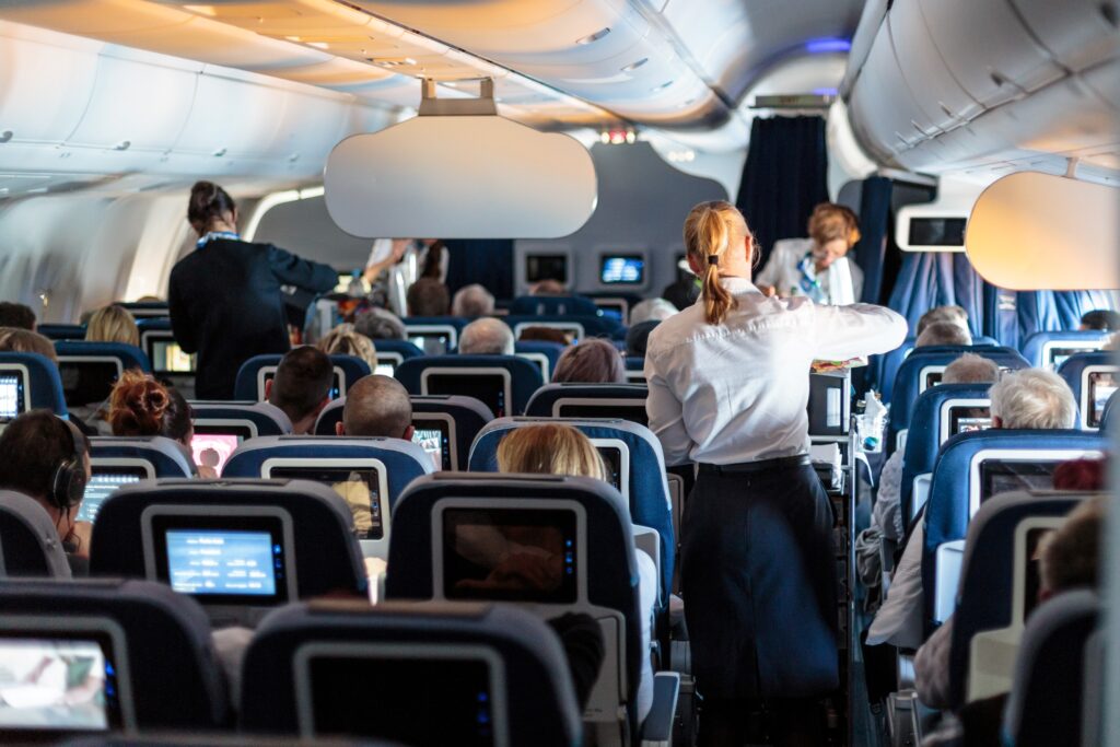 Flugbegleiterinnen schenken im Flugzeug an die sitzenden Passagiere Getränke aus.